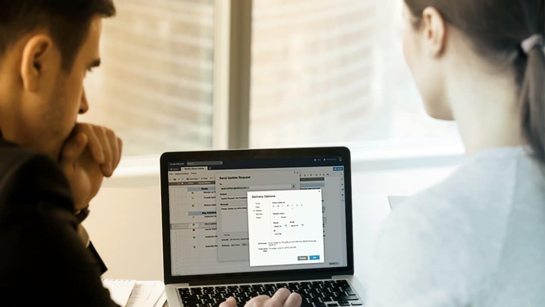 Two office workers manage Smartsheet automated alerts and actions.