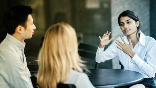 A businesswoman speaks to her colleagues at a table.